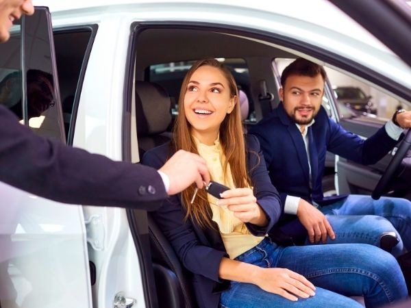 Happy young couple receiving car keys from dealer inside a modern car showroom, excited about new vehicle purchase
