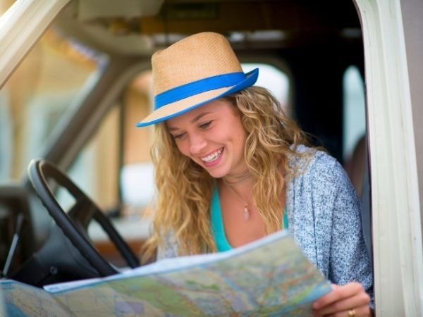Adventurous young woman in straw hat studying a road map inside a camper van, planning a road trip travel adventure
