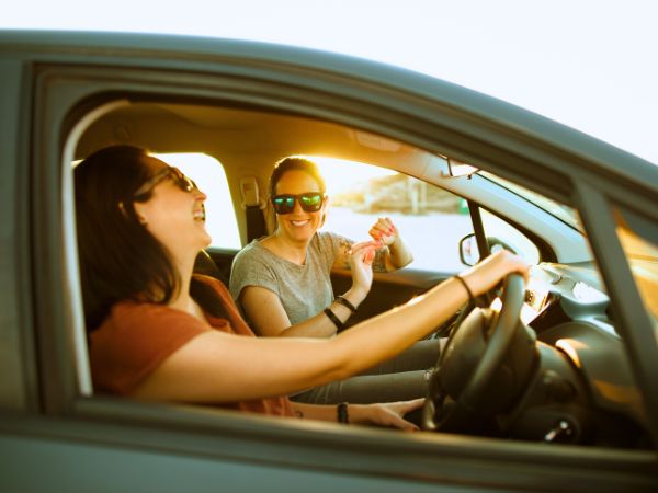 Two friends enjoying a scenic road trip in a rental car, with one woman driving and another passenger enjoying the journey.